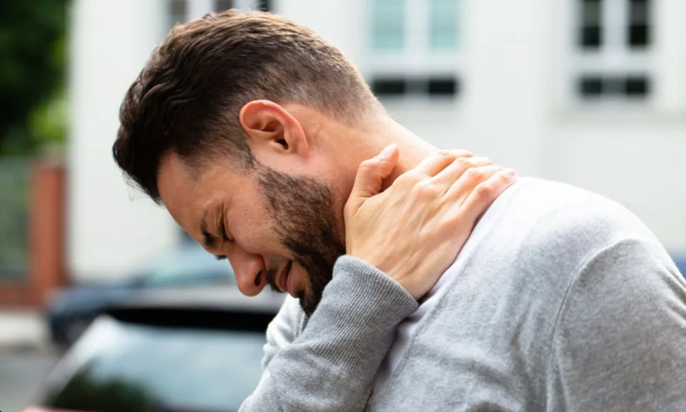 Man outdoors holding his neck, suggesting discomfort while recovering from a sports injury.