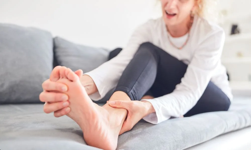 Woman on couch holding her foot, mirroring tension seen in chiropractic vs physio for neck pain.