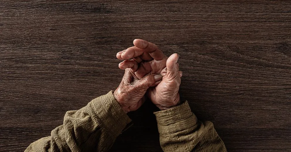 Elderly hands in a green shirt resting together, managing Parkinson’s Disease with care.