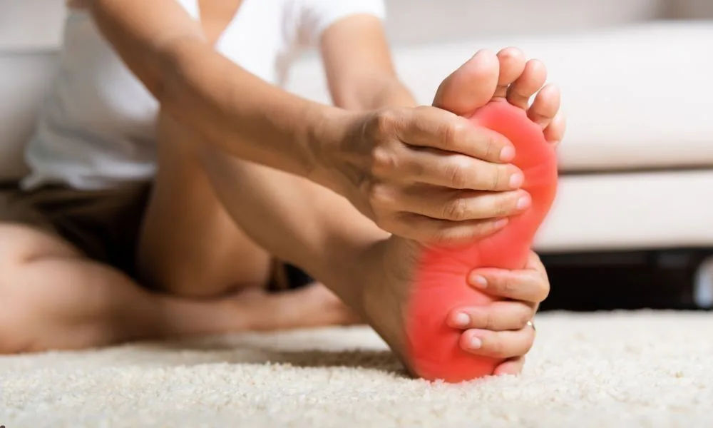 A person sits on the floor holding a red, painful foot, chiropractic care for back pain can help.