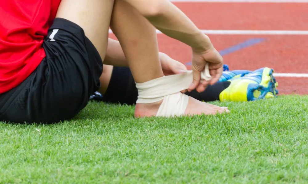 Person wrapping bandage around ankle, practicing occupational therapy for injury recovery outdoors.