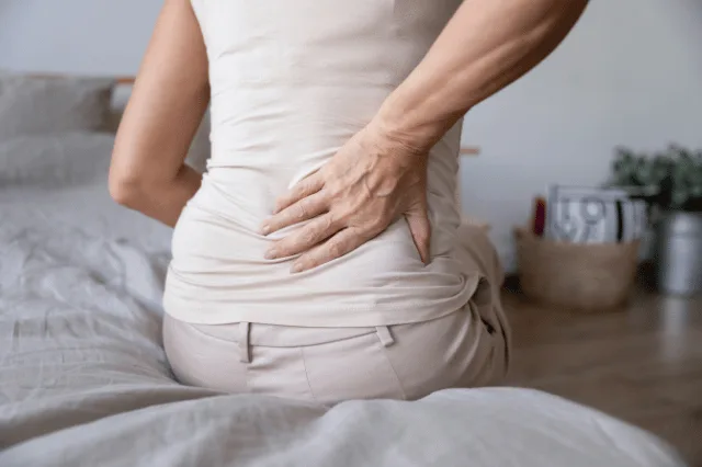 Female sitting on the bed holding her back in pain with sciatica