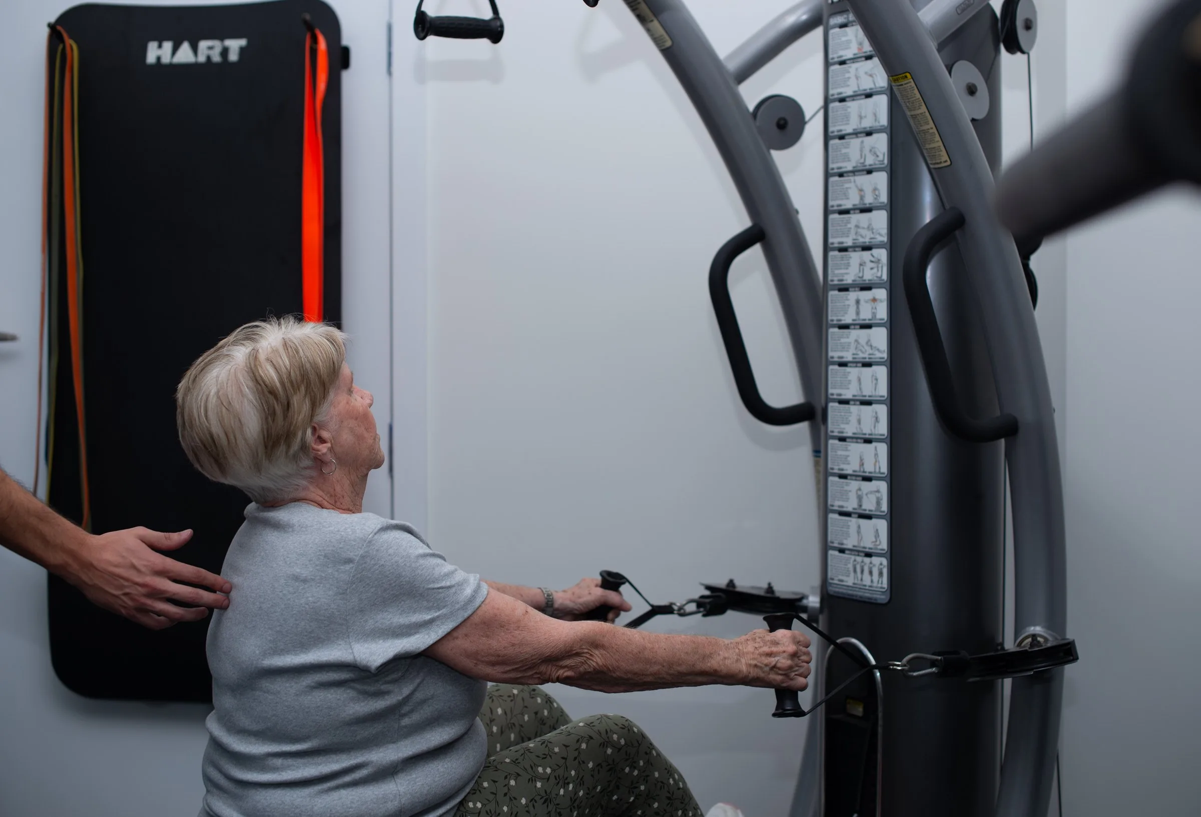 Patient rebuilding strength on the clinic equipment with a practitioner supporting her