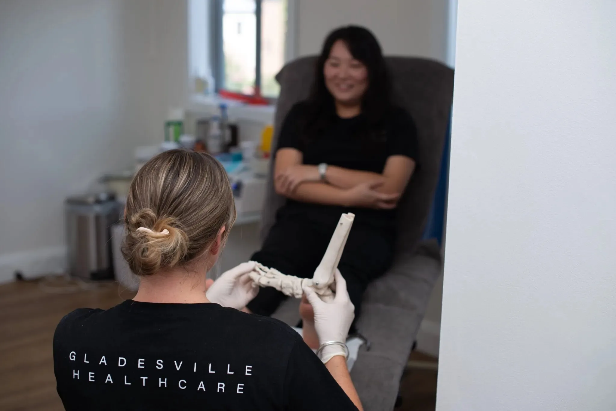 Podiatrist in a Gladesville Healthcare shirt using a foot model to explain a diagnosis to a patient