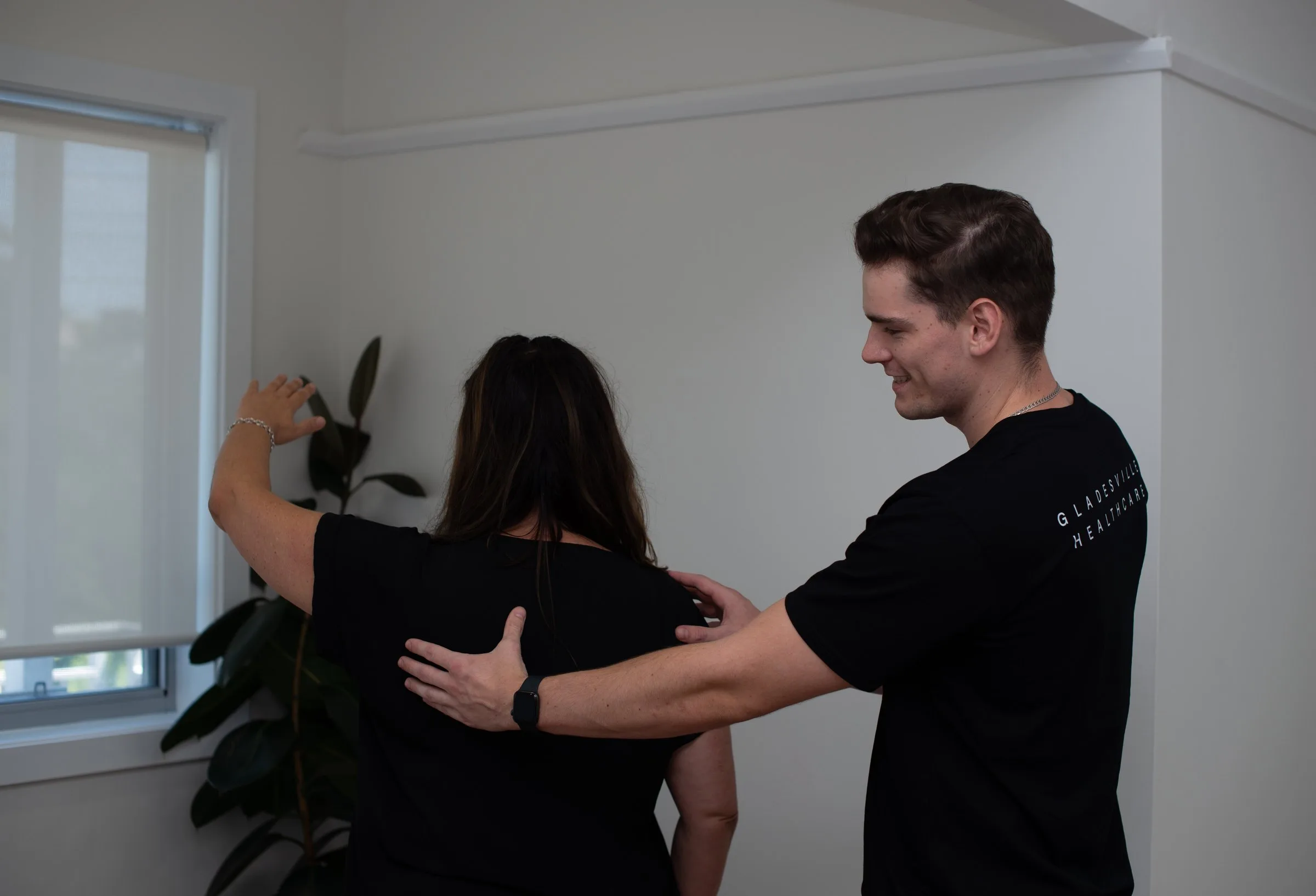 Practitioner applying pressure to a patient's shoulder while she raises her arm